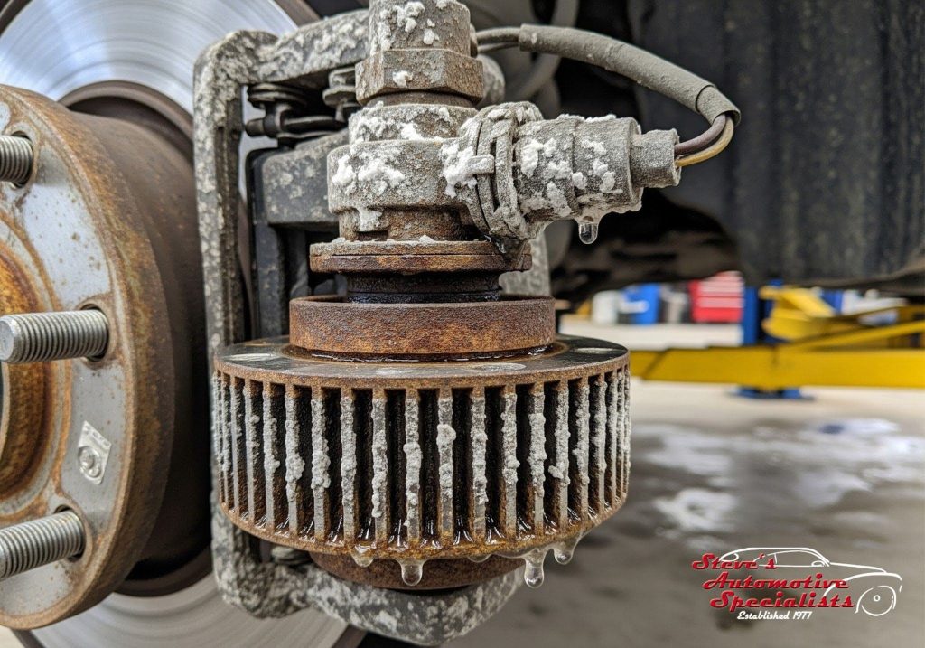 Close-up of a corroded ABS wheel speed sensor and magnetic tone ring damaged by road salt.