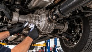 Mechanic inspecting a Land Rover rear differential and driveshaft with a flashlight during a professional driveline diagnostic inspection
